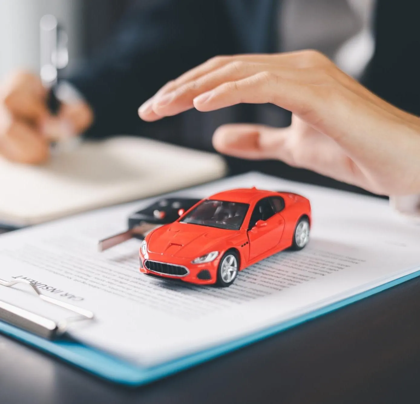 A hand held over a toy car resting on a policy document