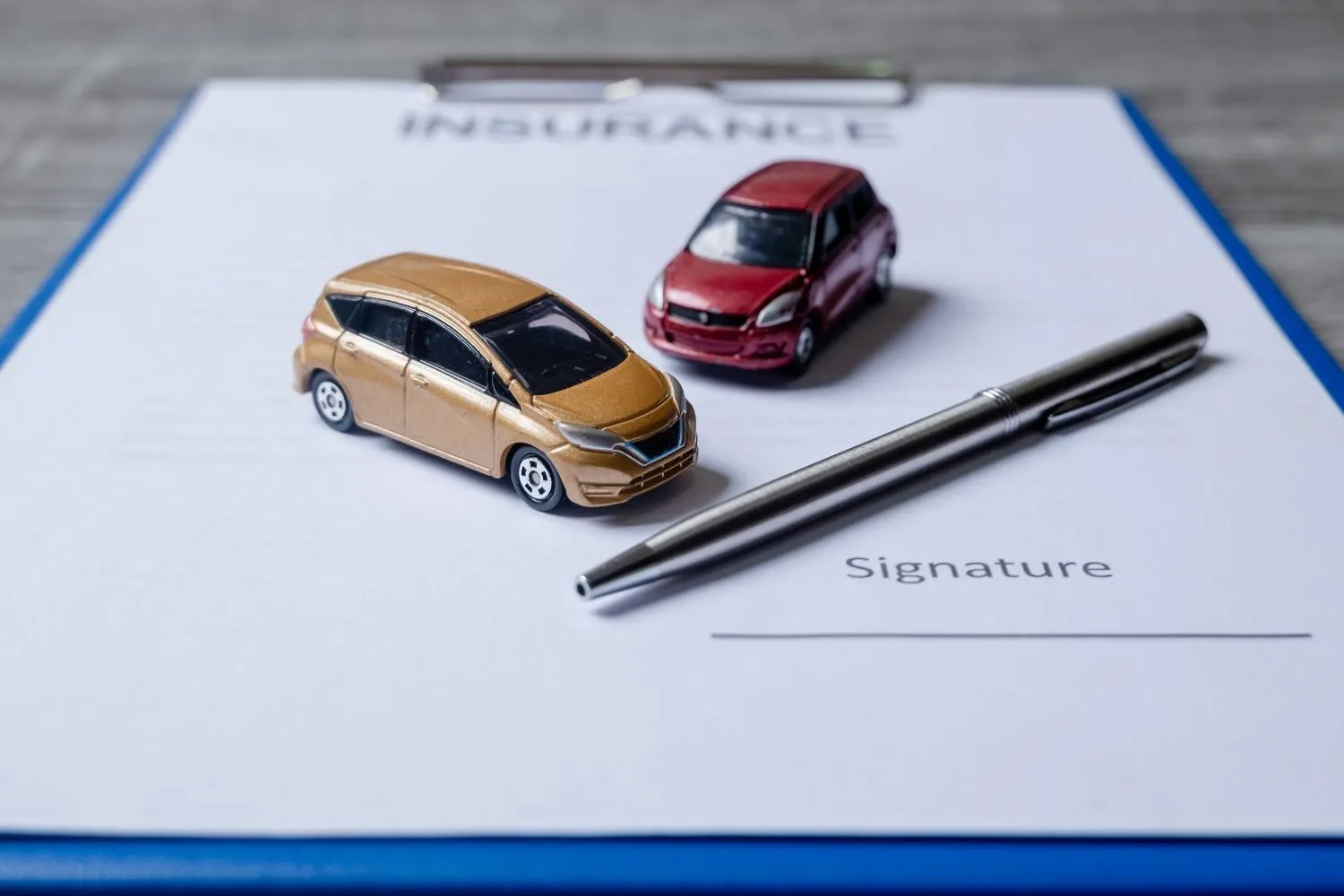 Two toy cars on an insurance form beside a pen